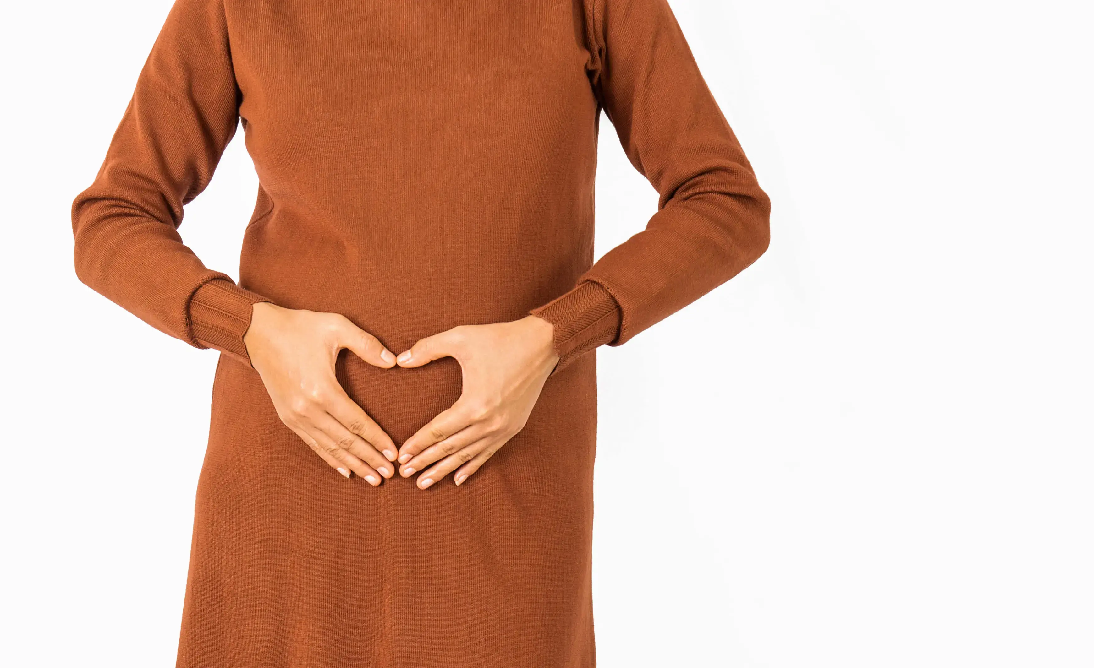 A woman making a heart shape with her hands, on her uterus